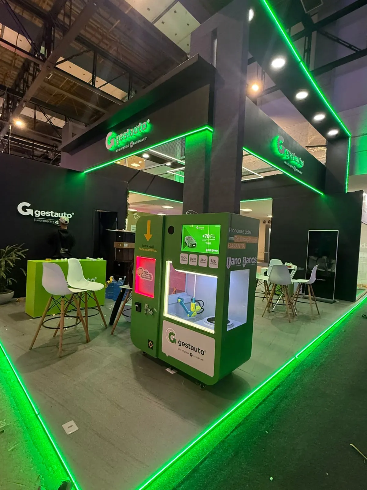 Máquina envelopada em verde com a identidade da Gestauto em um estande corporativo.
